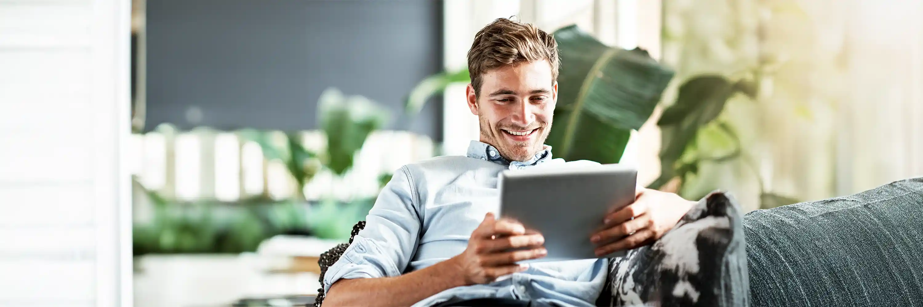 Man in a blue button down shirt is sitting and holding an ipad