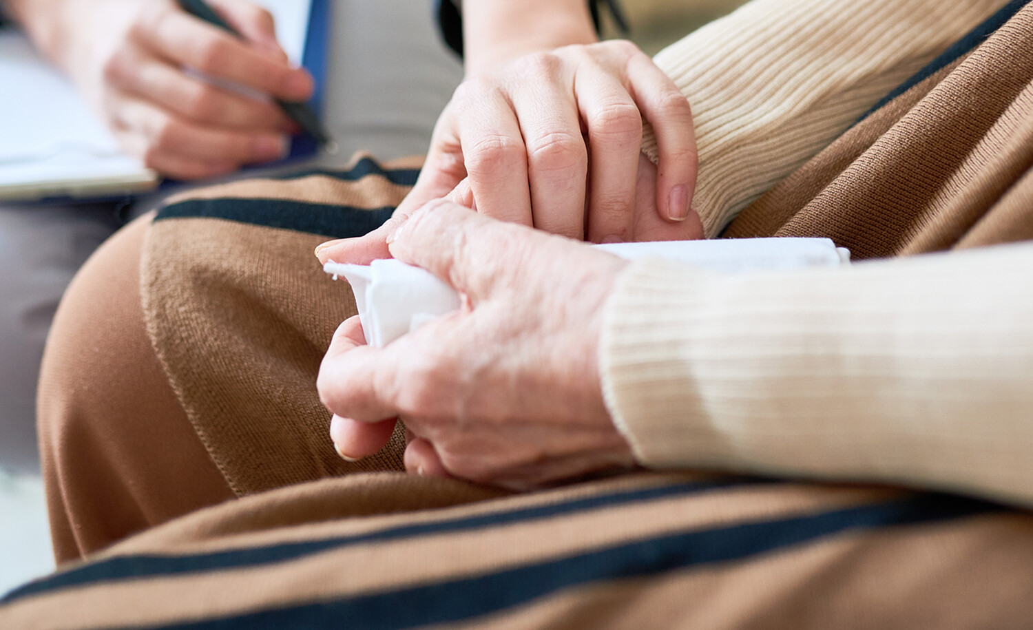 An person holding their hands clasped and some one offering a comforting hand.