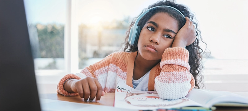A young girl looks off in a bored manner while sitting at a desk, representing ADHD symptoms of inattention in girls